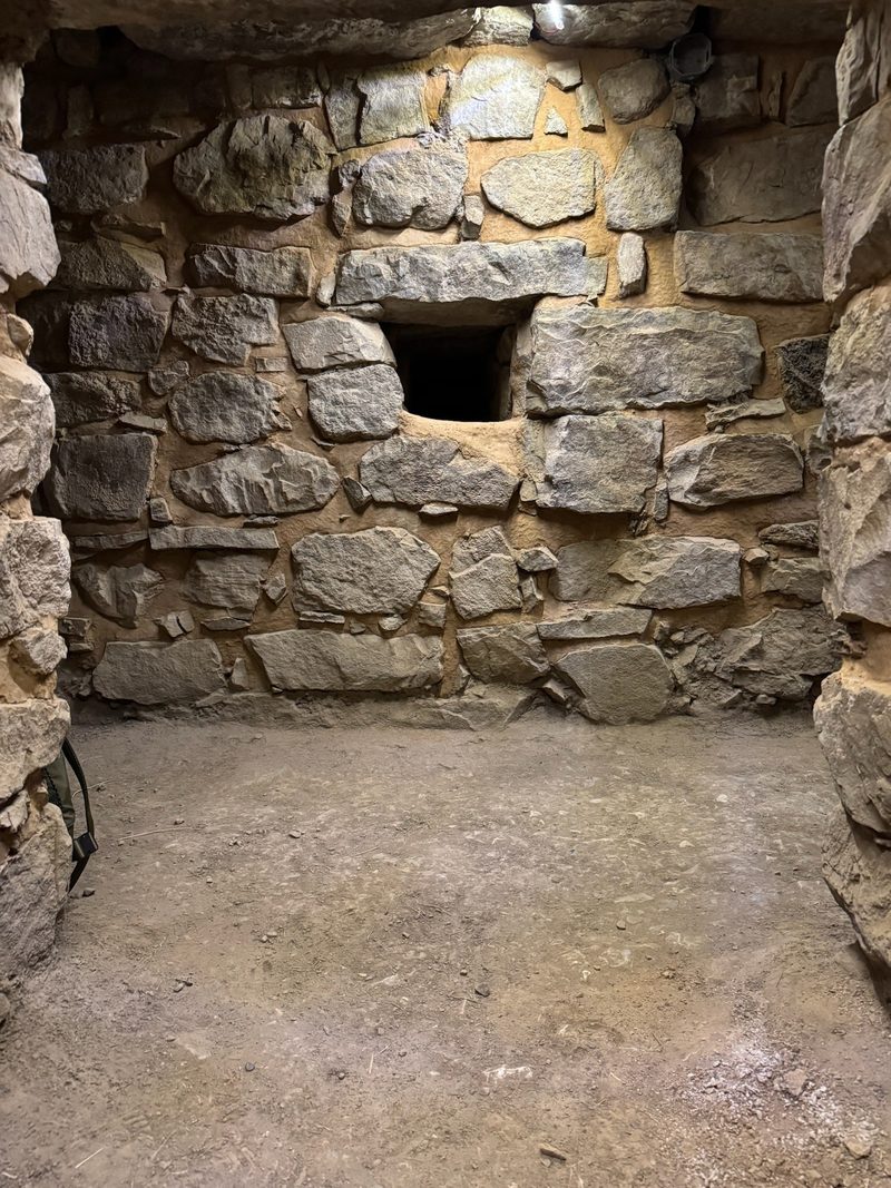 A small stone chamber in the galleries at Chavín de Huántar, a square opening set into the masonry wall above a bare earth floor